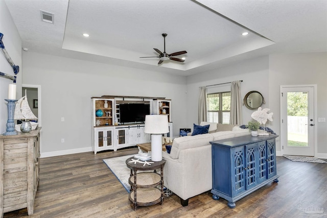 living room with dark wood-style floors, a raised ceiling, visible vents, and baseboards