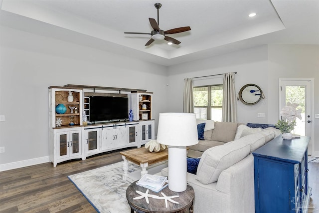 living area featuring ceiling fan, dark wood-type flooring, a raised ceiling, and baseboards