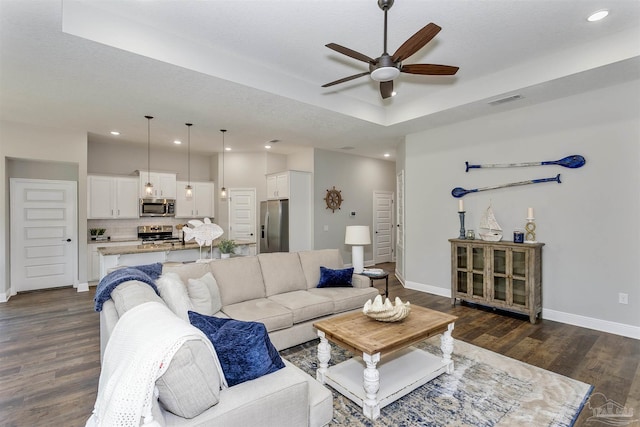 living area with dark wood-style flooring, recessed lighting, a raised ceiling, ceiling fan, and baseboards