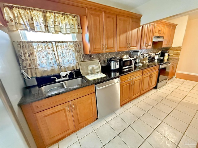 kitchen featuring appliances with stainless steel finishes, backsplash, dark stone counters, sink, and light tile patterned floors