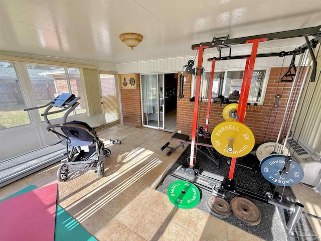 workout room with tile patterned flooring and brick wall