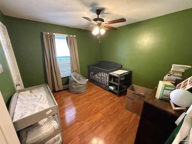 bedroom featuring ceiling fan, wood-type flooring, a textured ceiling, and a nursery area