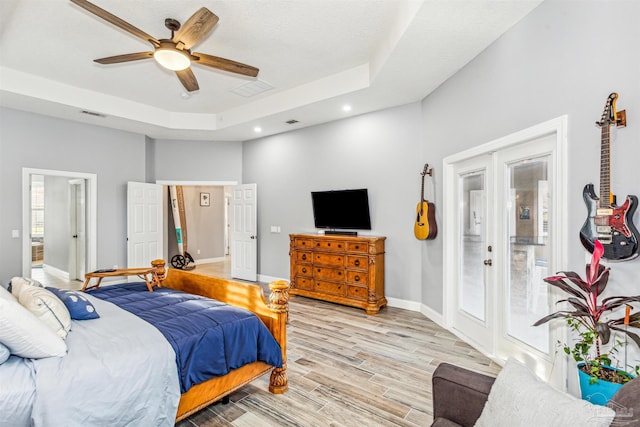 bedroom with french doors, a raised ceiling, ensuite bath, ceiling fan, and light hardwood / wood-style floors