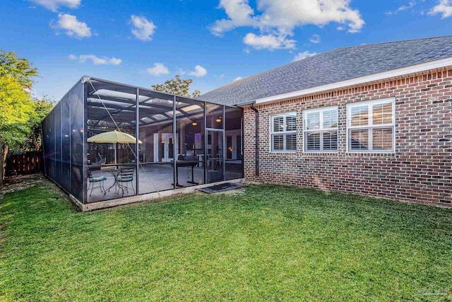 rear view of house with a lawn, glass enclosure, and a patio area