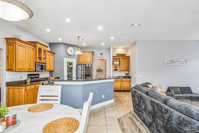 kitchen with an island with sink, a textured ceiling, decorative light fixtures, light tile patterned floors, and appliances with stainless steel finishes