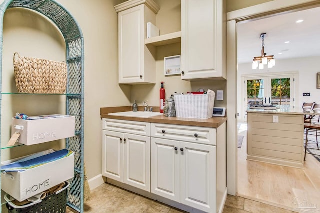 kitchen with white cabinets, light hardwood / wood-style floors, a notable chandelier, and sink