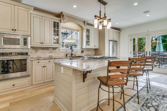 kitchen featuring light stone countertops, stainless steel appliances, decorative light fixtures, light hardwood / wood-style flooring, and a kitchen island