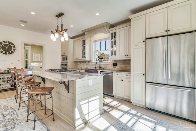 kitchen with light stone countertops, light hardwood / wood-style flooring, decorative light fixtures, a kitchen island, and appliances with stainless steel finishes