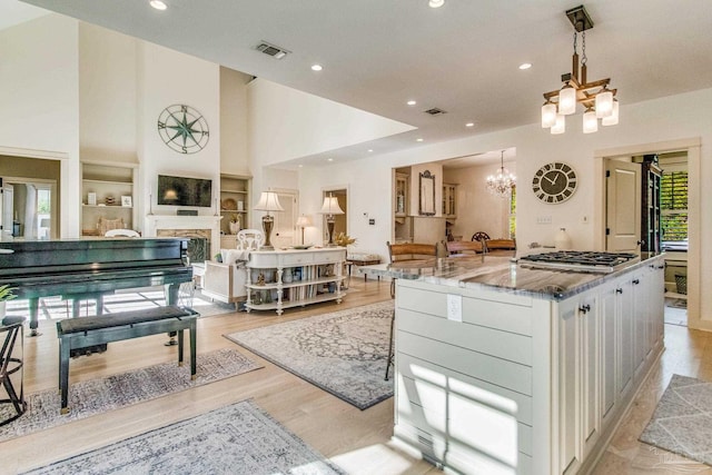 kitchen with light stone countertops, stainless steel gas cooktop, light hardwood / wood-style flooring, an inviting chandelier, and white cabinets