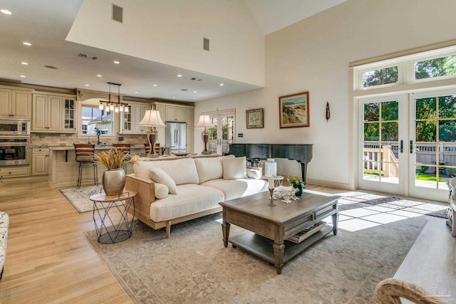 living room featuring light hardwood / wood-style flooring, a high ceiling, a wealth of natural light, and french doors