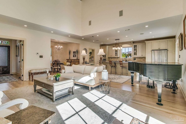 living room with a towering ceiling, light hardwood / wood-style floors, and an inviting chandelier