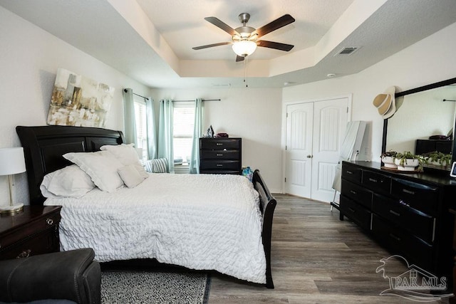 bedroom featuring a closet, a raised ceiling, hardwood / wood-style floors, and ceiling fan