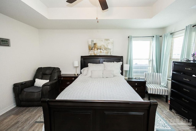 bedroom with ceiling fan, light wood-type flooring, and a raised ceiling