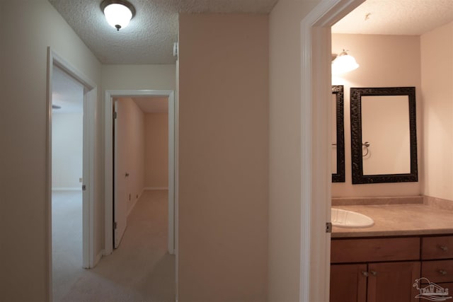 hall featuring sink, light colored carpet, and a textured ceiling