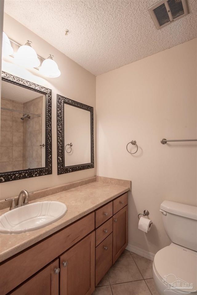 bathroom with vanity, a tile shower, a textured ceiling, tile patterned floors, and toilet