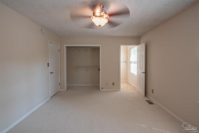 unfurnished bedroom with a textured ceiling, light colored carpet, a closet, and ceiling fan