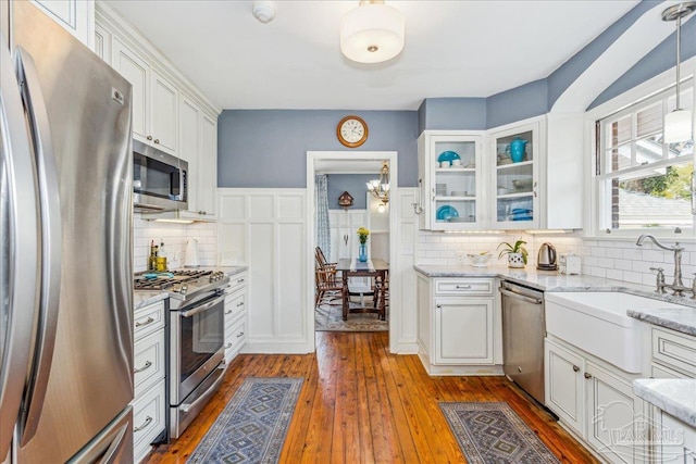 kitchen with white cabinets, hardwood / wood-style flooring, glass insert cabinets, light stone countertops, and stainless steel appliances