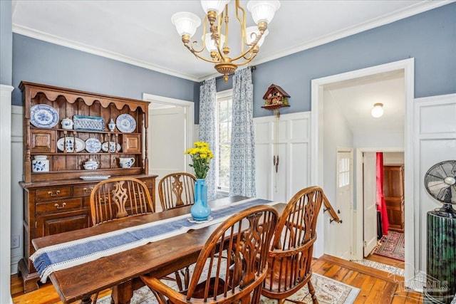 dining area with ornamental molding, wood finished floors, and an inviting chandelier