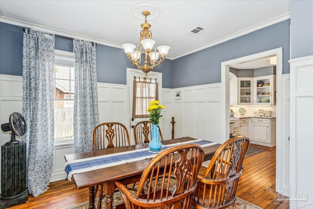 dining space with a chandelier, wainscoting, visible vents, and crown molding