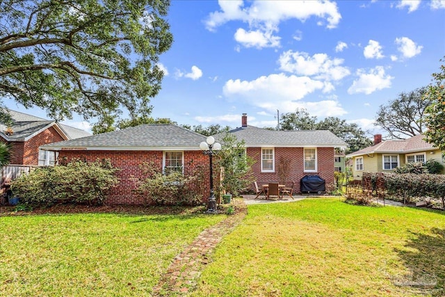 back of house with a patio, brick siding, a lawn, and a chimney