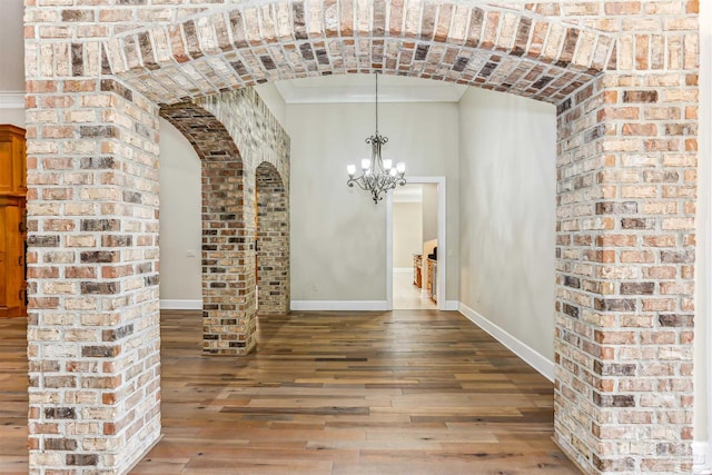unfurnished dining area with arched walkways, hardwood / wood-style floors, baseboards, and an inviting chandelier