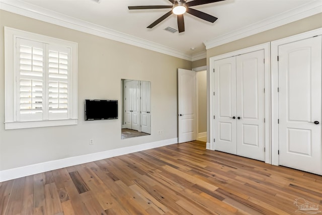 unfurnished bedroom featuring wood finished floors, visible vents, crown molding, and baseboards