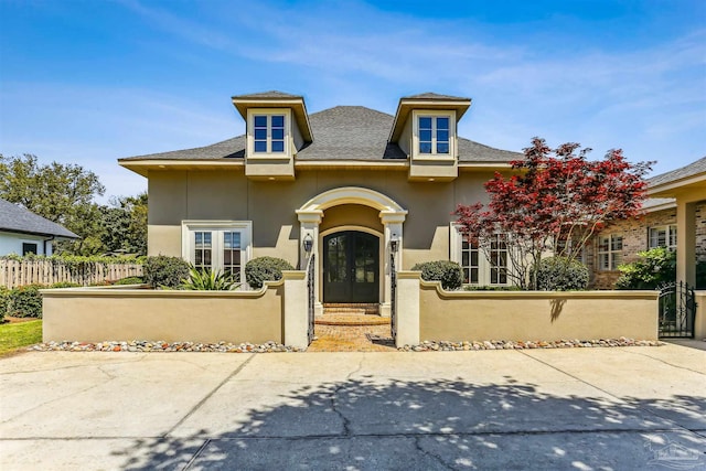 view of front of property featuring french doors, a fenced front yard, roof with shingles, and stucco siding