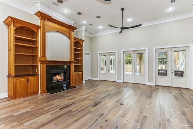 unfurnished living room featuring a ceiling fan, ornamental molding, french doors, light wood-type flooring, and a large fireplace