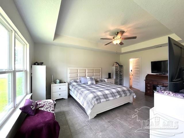 bedroom with multiple windows, ceiling fan, a raised ceiling, and a textured ceiling