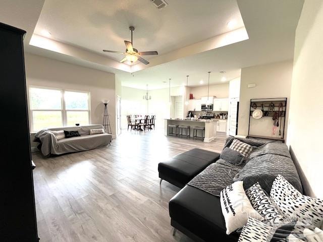 living room featuring a raised ceiling, ceiling fan, and light hardwood / wood-style flooring