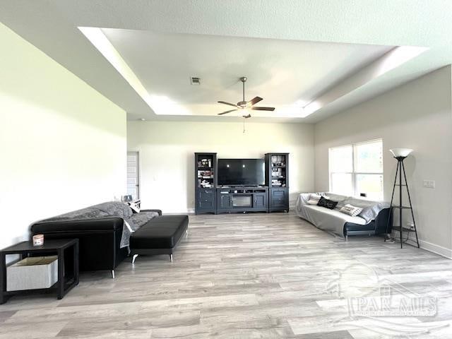 living room with a raised ceiling, a textured ceiling, ceiling fan, and light hardwood / wood-style floors