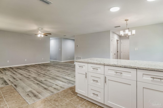 kitchen with light wood-type flooring, pendant lighting, light stone countertops, ceiling fan with notable chandelier, and white cabinets