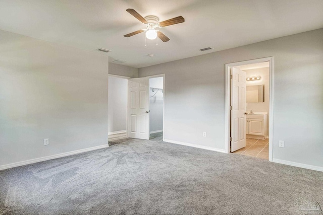 unfurnished bedroom with ensuite bath, a walk in closet, light colored carpet, and ceiling fan