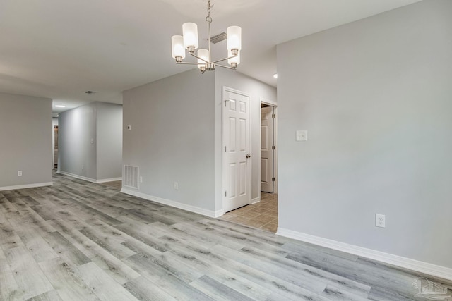 spare room featuring an inviting chandelier and light hardwood / wood-style floors