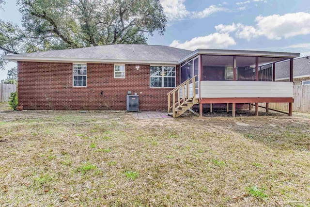 rear view of property featuring central air condition unit, a sunroom, and a lawn