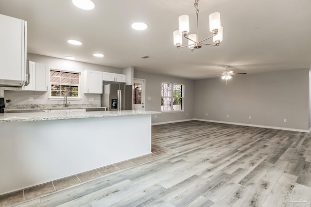 kitchen featuring pendant lighting, stove, light stone counters, white cabinets, and stainless steel fridge with ice dispenser