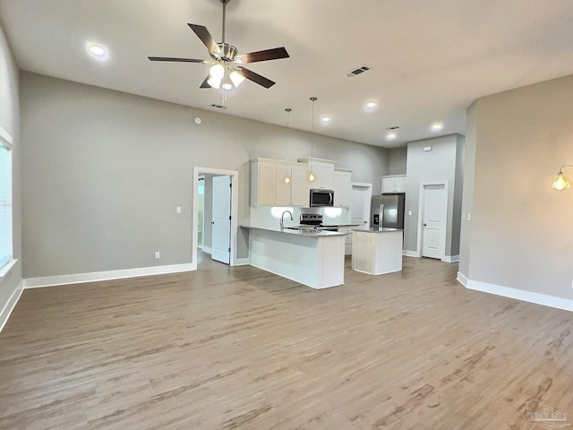 kitchen with white cabinets, hanging light fixtures, a kitchen island with sink, stainless steel appliances, and light wood-type flooring