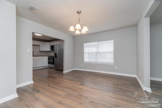 unfurnished dining area with baseboards, wood finished floors, visible vents, and an inviting chandelier