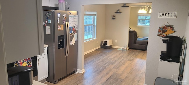 kitchen featuring wood finished floors, stainless steel fridge, white cabinetry, and pendant lighting