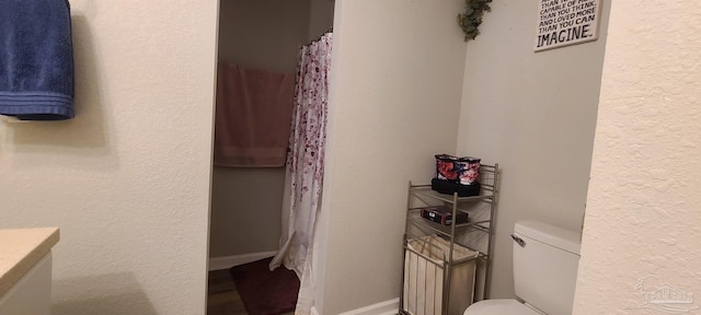 bathroom with a textured wall, vanity, toilet, and baseboards