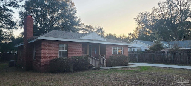 view of front of house with brick siding, a chimney, central AC unit, and fence