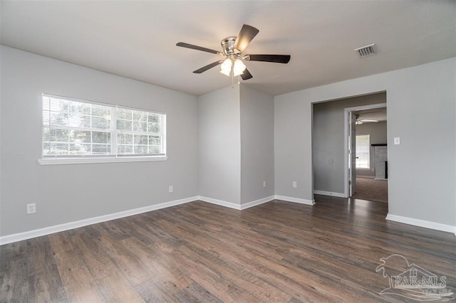 spare room featuring dark wood-style floors, a brick fireplace, visible vents, and ceiling fan