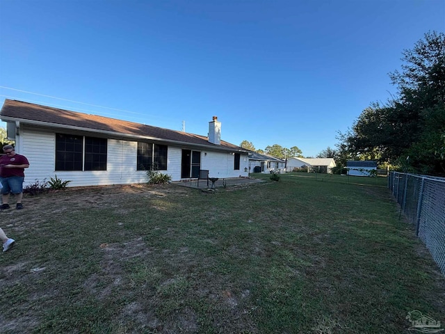 rear view of house with a chimney, a lawn, a patio, and fence