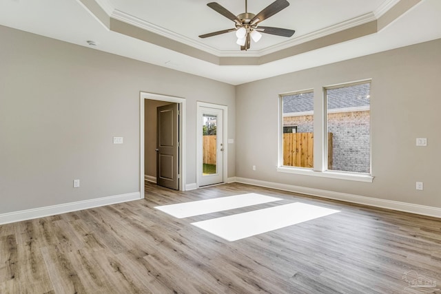 empty room with a tray ceiling, ceiling fan, light hardwood / wood-style floors, and ornamental molding