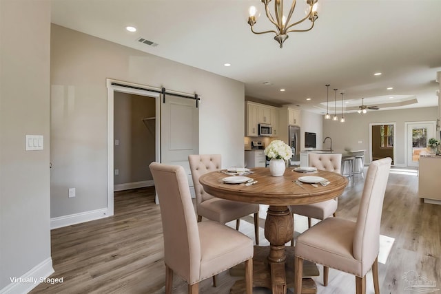 dining space with ceiling fan with notable chandelier, a barn door, light hardwood / wood-style floors, and sink