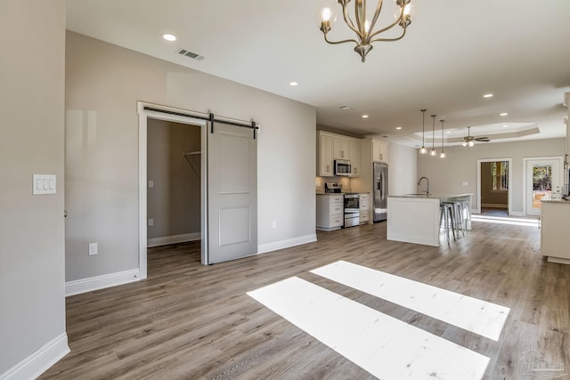 unfurnished living room with ceiling fan with notable chandelier, a barn door, light hardwood / wood-style floors, and sink