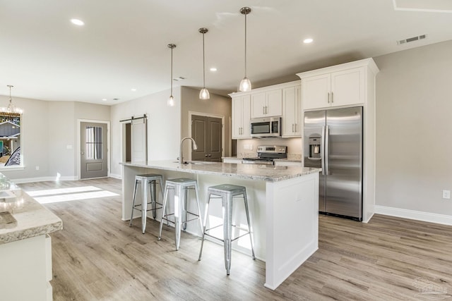 kitchen with pendant lighting, a kitchen island with sink, white cabinets, a barn door, and stainless steel appliances