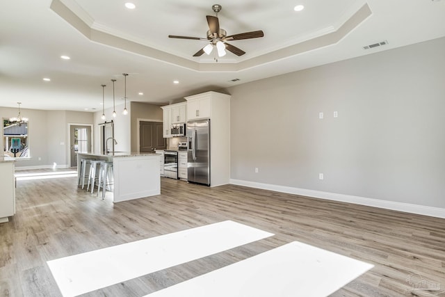 kitchen featuring white cabinets, appliances with stainless steel finishes, light hardwood / wood-style flooring, and an island with sink