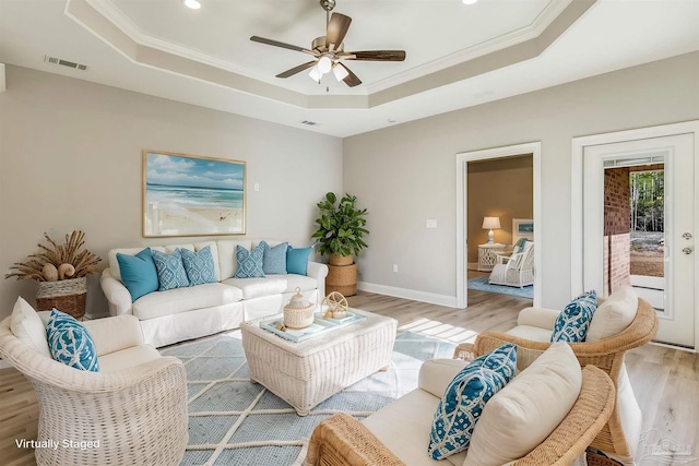 living room with ceiling fan, a raised ceiling, crown molding, and light hardwood / wood-style flooring