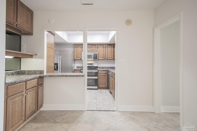 kitchen with appliances with stainless steel finishes, a tray ceiling, and light tile patterned floors